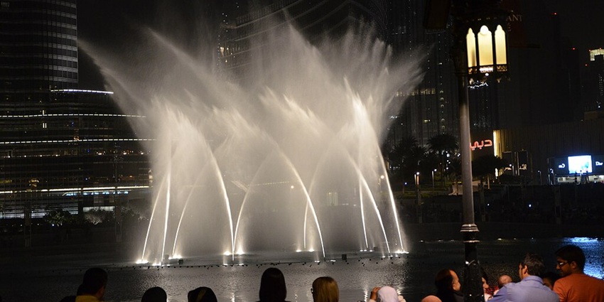 Crowd watching Dubai Fountain show at night with illuminated water jets and city lights.