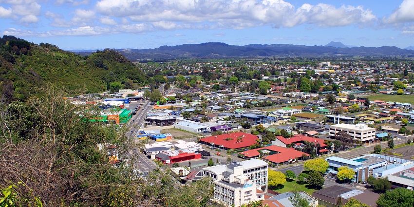 Scenic view of Whakatane town with buildings, greens, and hills in the backdrop.