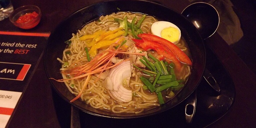 Pork thukpa with noodles, spring onions, onion and boiled egg served in a black bowl