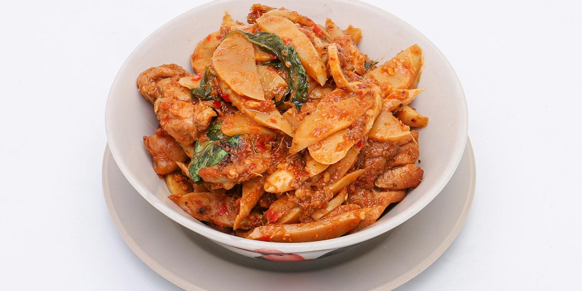 Chicken garnished with green leaves and chilli paste served in a white ceramic bowl.
