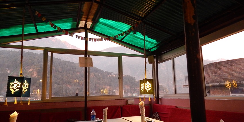 Inside a restaurant in mcleodganj with napkins and bottles on each table and hanging lamps