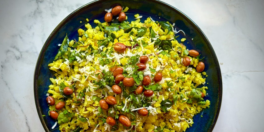 Poha garnished with peanuts and coriander leaves served on a blue plate