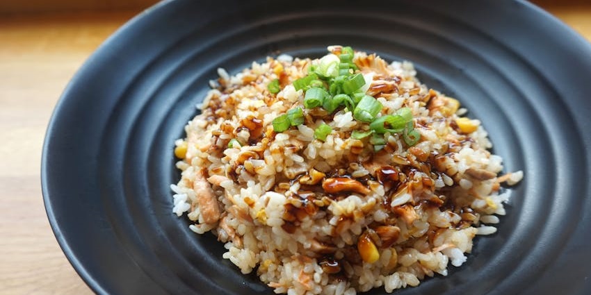 Fried rice with rice, vegetables, soy sauce and spring onions on top, served on a black plate