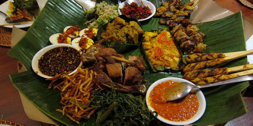 A banana leaf filled with assorted Balinese cuisine, featuring vibrant and flavorful dishes.