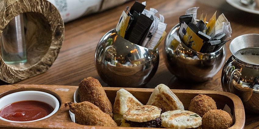 A tray with Sri Lankan short eats and sauce, on a table with condiments in the background