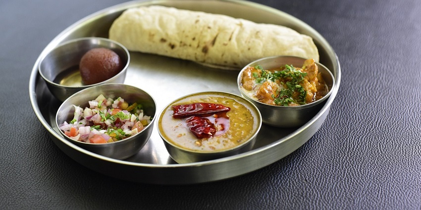 Vegetarian thali with two Kashmiri chillies on curry served alongside salad and dessert