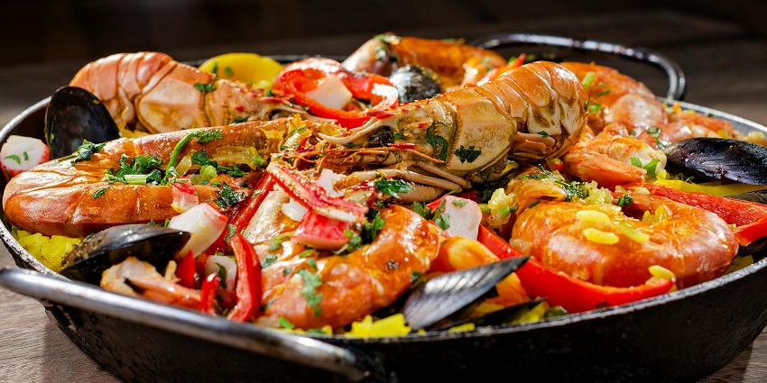 Colourful seafood paella with prawns, mussels, and vegetables in a large black pan.