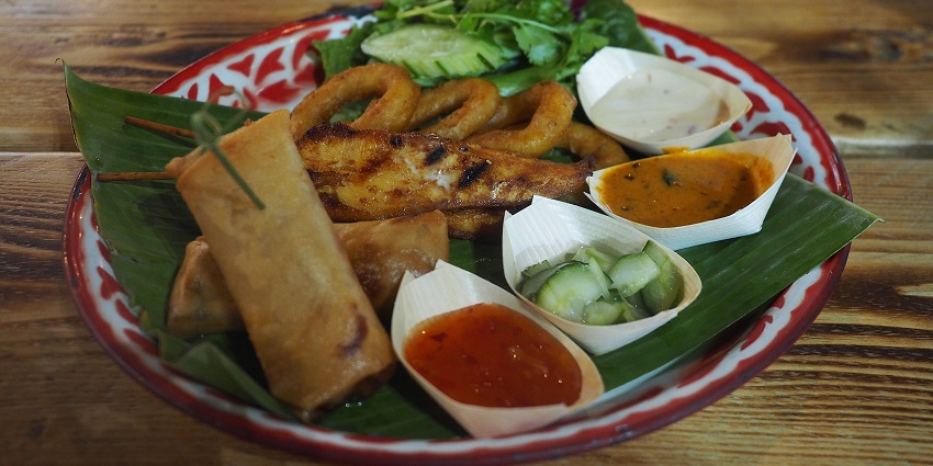 Traditional Balinese platter at Canggu Beach café with satay, spring rolls, and sauces.