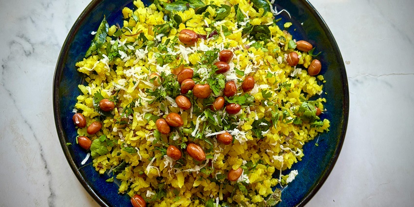 Image of Indian food yellow Poha served on a plate with peanuts and green leaves toppings