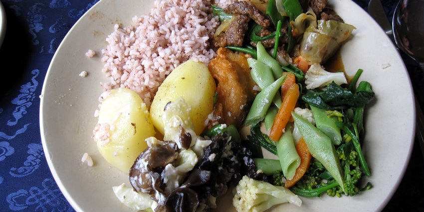 A traditional Bhutanese meal on a wooden table in Chorten Bhutan, featuring Ema Datshi, red rice, and dumplings.