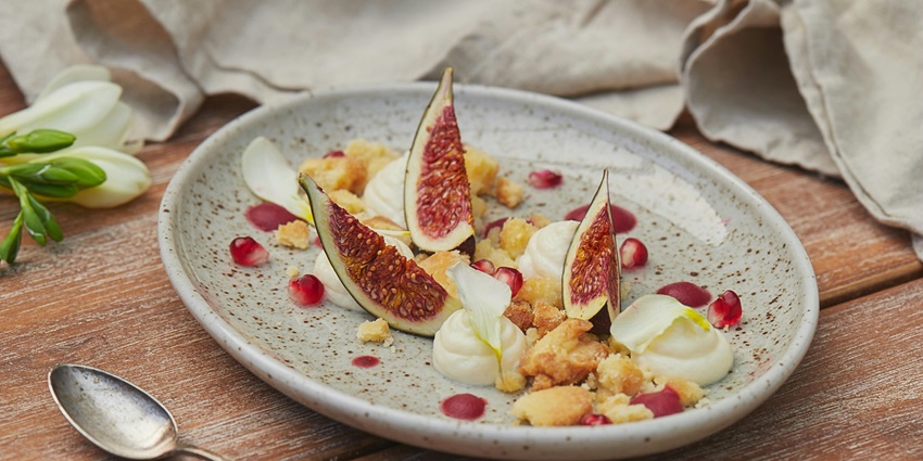 Gourmet dessert with fresh fig slices, cream dollops, crumbles, and pomegranate seeds