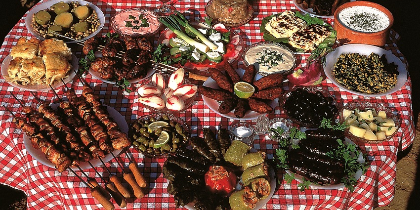 Different types of dishes spread on a red and white mat over a table under the sunlight.