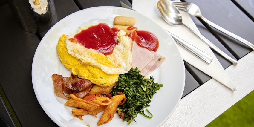 Serving breakfast plate with an omelet with ketchup, pasta, bacon, ham, and spinach.