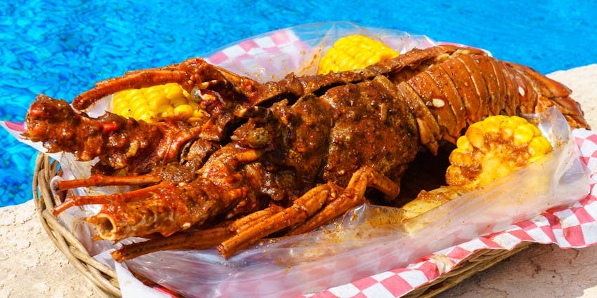 Grilled lobster with multiple sweet corn pieces served in a brown basket and pool in the back