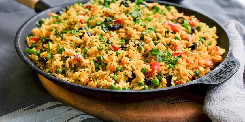Vegetable rice dish with peas, bell peppers, olives, and herbs served in a black skillet