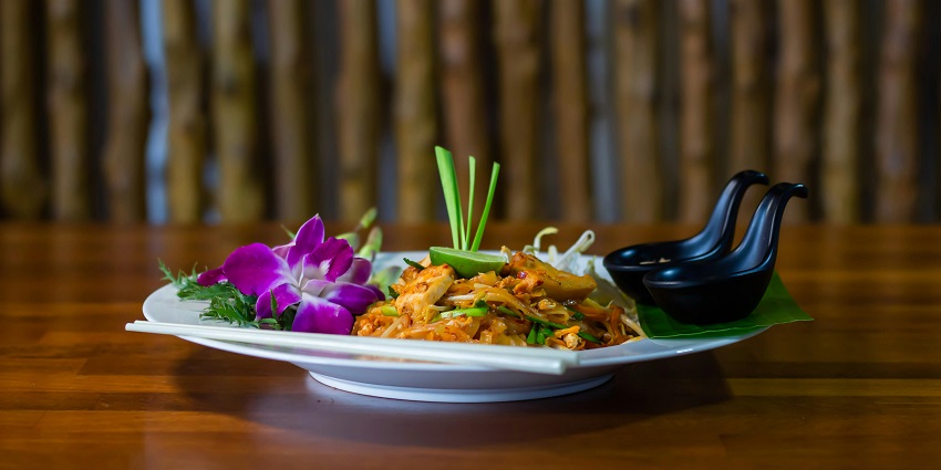 Elegant plate of Pad Thai garnished with fresh herbs, lime, served with chopsticks