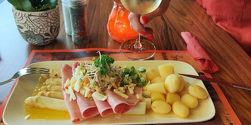 A plate of Asperges Limbourgoise with white asparagus, ham, eggs, and creamy sauce.