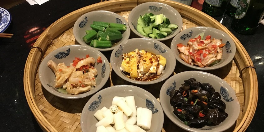 A traditional Chinese meal being served in small bowls on a woven bamboo tray.
