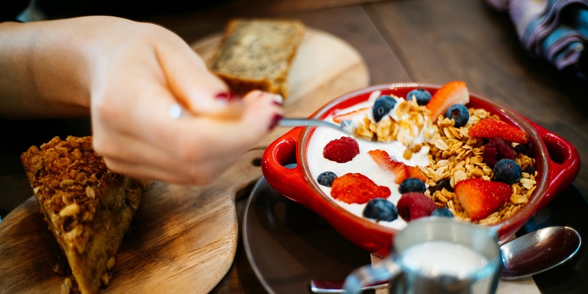 A person eating a yogurt parfait with granola, strawberries, blueberries, and raspberries