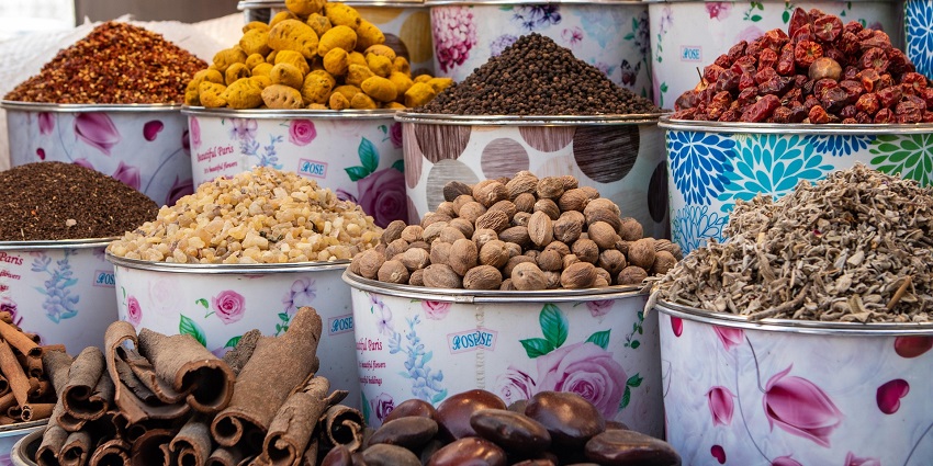 Display of assorted spices, herbs, and dried goods in floral containers at a market.