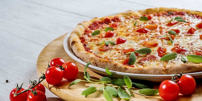 baked pizza with tomatoes, cheese, and herbs on a wooden board with cherry tomatoes