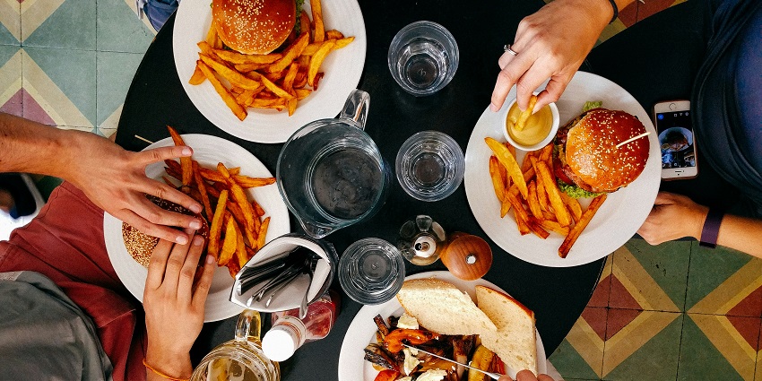 Image of a group of people eating burgers, fries and other sides drinks - food served on a round table