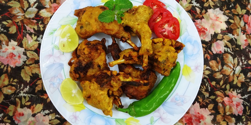 Kashmiri dish Kabargah with chicken, a big green chilli and tomato served on a white plate