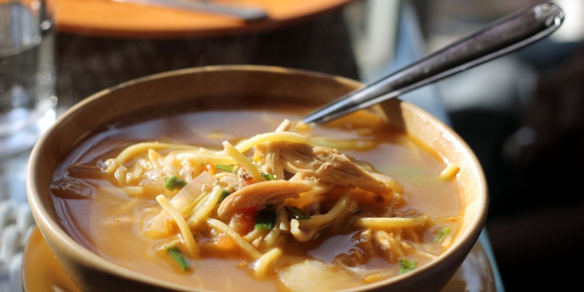 Thukpa with different vegetables in a noodle soup, a spoon served in a brown bowl