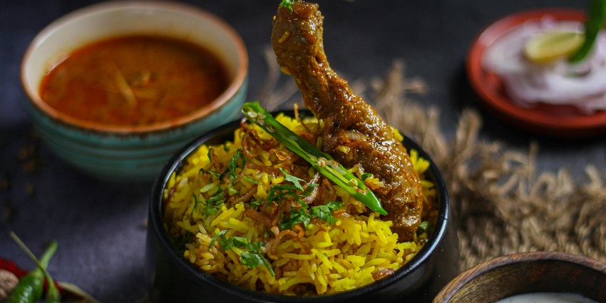 A bowl of chicken biryani with a chicken leg piece on top, garnished with green chilies