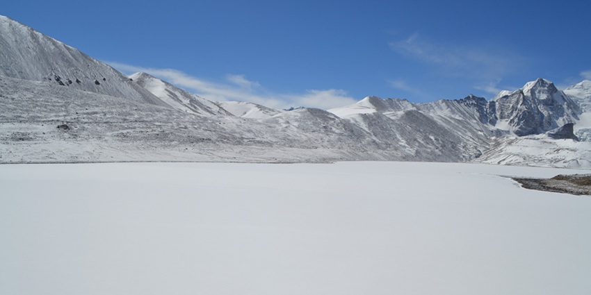 Peaceful panorama of Gurudongmar Lake in December, set amidst snow-clad mountains.