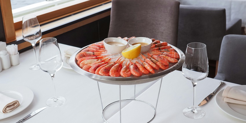 A seafood platter with shrimp, sauces, and lemon, served on a table with white linens.