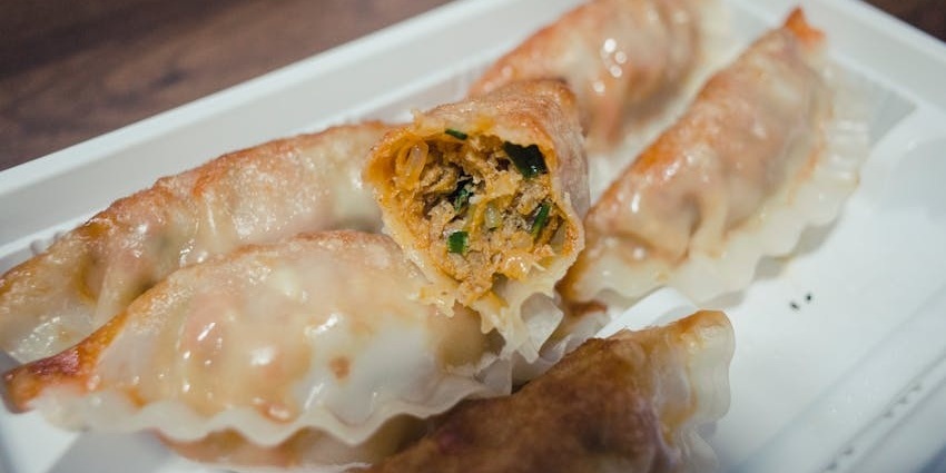 Close-up of pan-fried dumplings on a white rectangular plate, with one dumpling split open