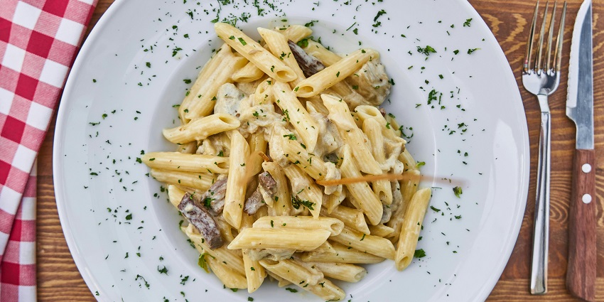 An image of mouth-watering cream cheese pasta on a white plate at a restaurant.