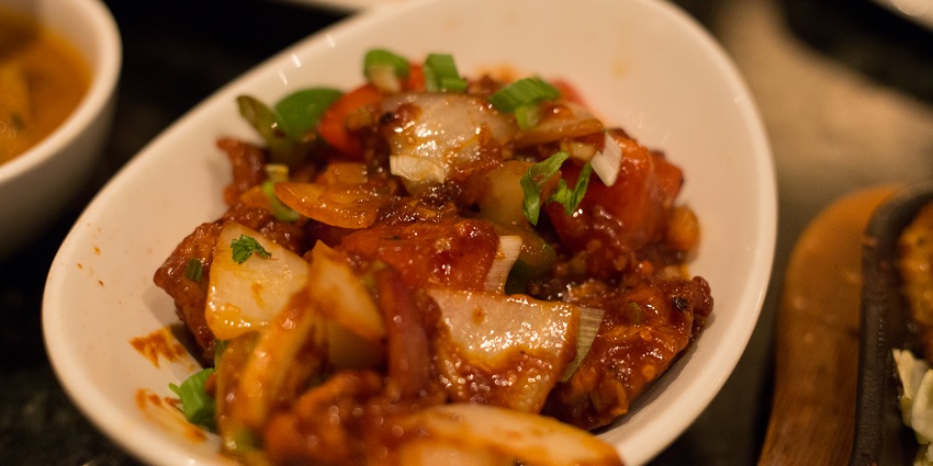 A close-up of an Indo-Chinese dish served in a white bowl, garnished with fresh herbs