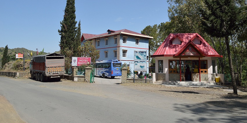 Truck and a bus parked outside the Hotel Bhagal, QuickBites store and tall trees beside