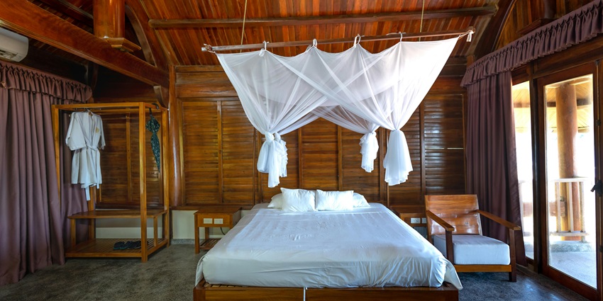 Interior of a resort with a bedroom, wooden walls, wooden furniture and white curtains