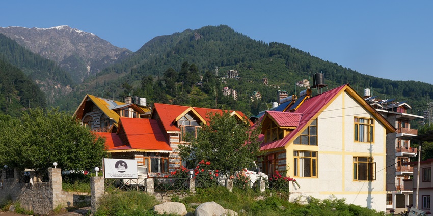 White and red cottage nestled among vibrant green mountains and dense forest trees