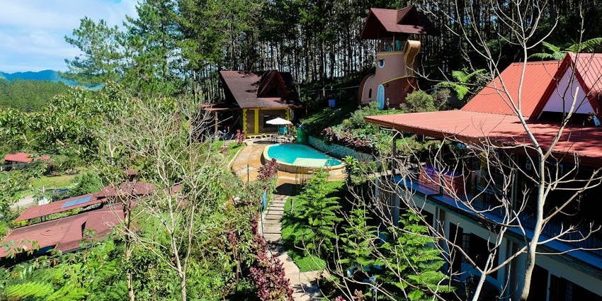 Resort with a small pool, multiple buildings of the resort surrounded by trees and hills