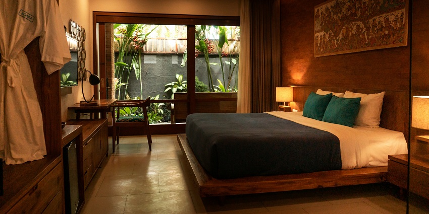 A cosy hotel room with a wooden bed, warm lighting, and a garden view through glass doors.