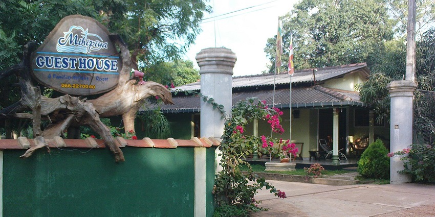 Entrance of Mihipiya Guesthouse with a rustic sign, flowers, and a cozy verandah view