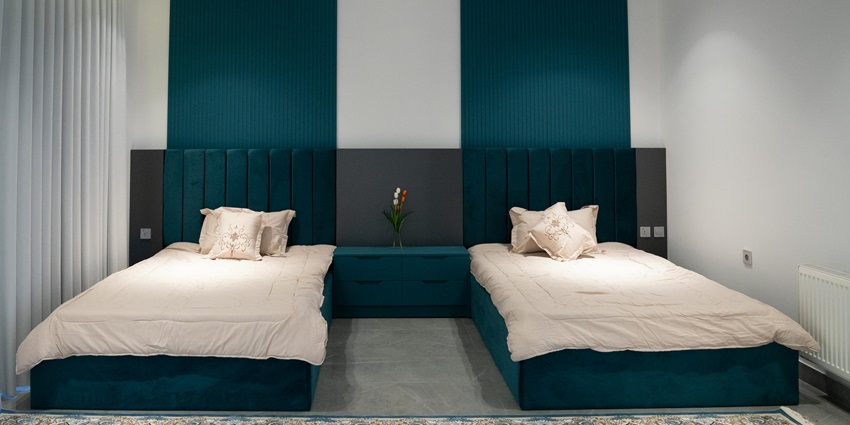 Modern bedroom with two single beds, teal headboards, and a nightstand with flowers.