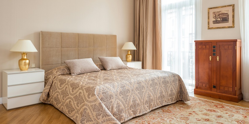 Elegant bedroom with beige tones, a large bed, wooden cabinet, and natural light.
