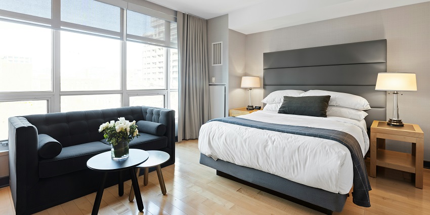 Modern hotel room near Canggu Beach with a cozy bed, sofa, and large city-view windows.