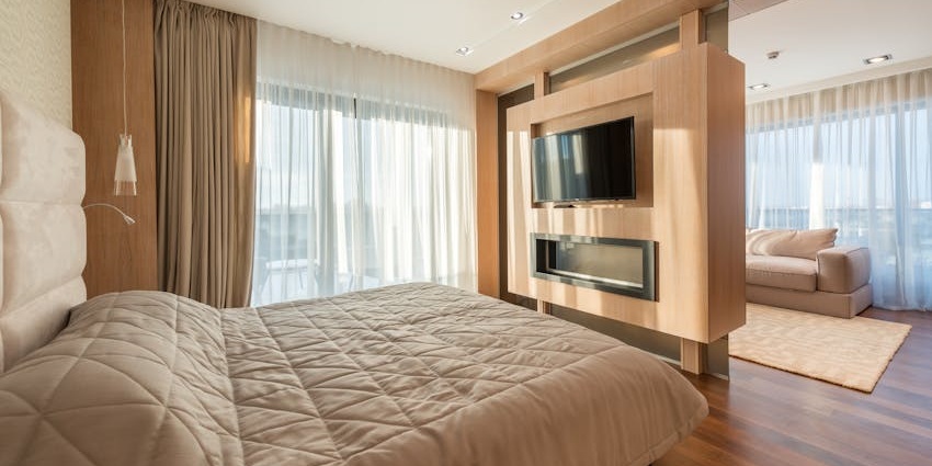 Modern bedroom with beige tones, featuring a bed, mounted TV, and a cosy sitting area