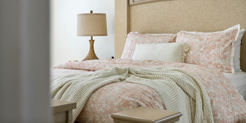Cosy bedroom with a beige headboard, soft pink bedding, and a knitted cream blanket.