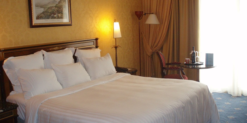 A cosy hotel room with a neatly made bed with white linens and multiple pillows.