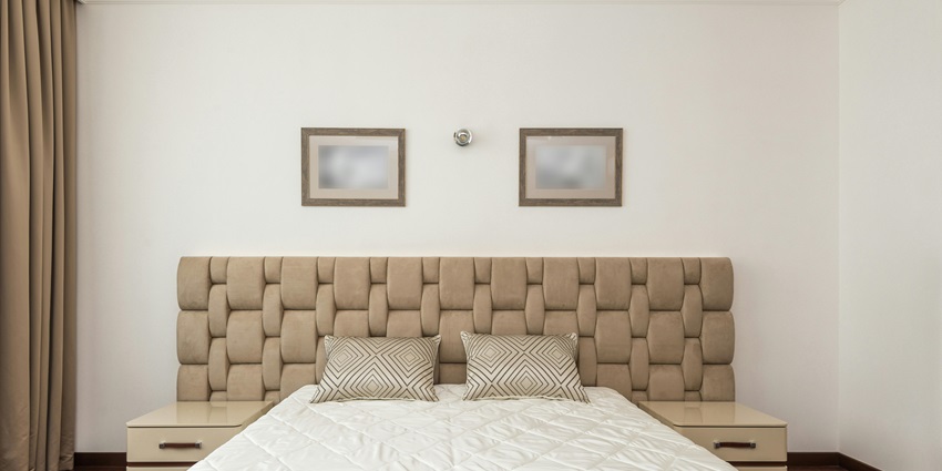 Bedroom with a beige padded headboard, geometric pillows, and a white quilted bedspread.