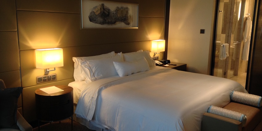 A cosy and modern hotel room with a neatly made bed, accent pillows, and warm lighting