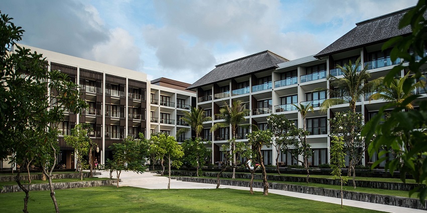 Resort with greenery, palm trees, and contemporary architecture under a cloudy sky.