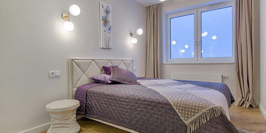 An image of a bedroom featuring a padded headboard, purple decor, and artistic lighting